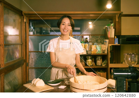 在老民居的廚房裡，一位中年婦女正在綁飯糰。 120642880