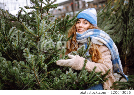 A young smiling woman chooses a Christmas tree to buy. Holiday concept, shopping. A young smiling woman chooses a Christmas tree to buy. Holiday concept, shopping. 120643036