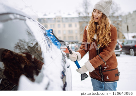 Portrait of young woman cleaning snow off car during winter snowfall. Winter, vehicle concept. Portrait of young woman cleaning snow off car during winter snowfall. Winter, vehicle concept. 120643096