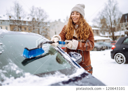Portrait of young woman cleaning snow off car during winter snowfall. Winter, vehicle concept. 120643101