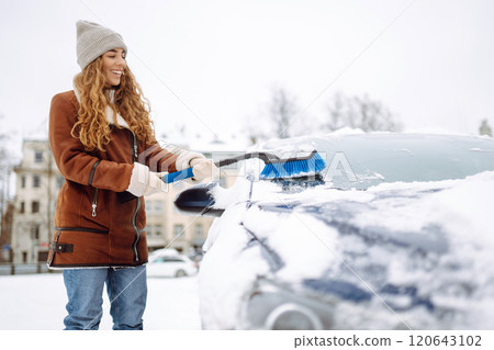 Beautiful woman is cleaning snow from a car with a brush. Transport concept, seasonality 120643102