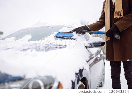 Transport, winter, weather, people and vehicle concept - young man cleaning snow from car with brush 120643254