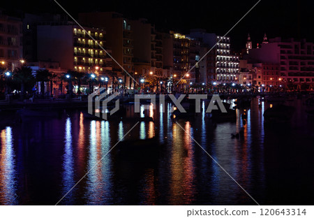 Waterfront promenade at night with colorful reflections of illuminated buildings and lights on water Waterfront promenade at night with colorful reflections of illuminated buildings and lights on water 120643314