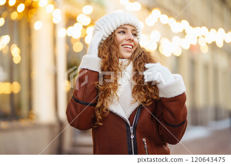 A young woman walks through a Christmas market decorated with festive decorations and lights. 120643475