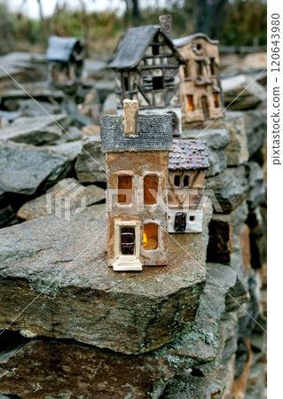 New trends in garden and interior decoration: ceramic houses with glowing windows in modern style. Garden ceramics, miniature. The house placed on old stone wall against rural landscape. Cloudy day. 120643980