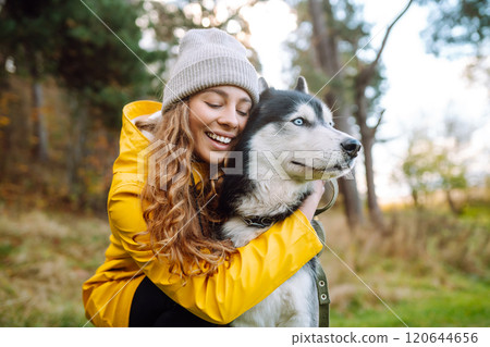 Beautiful young woman in a hat and yellow coat walks with her husky on the lawn in the park. 120644656
