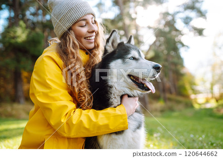 Beautiful young woman in a hat and yellow coat walks with her husky on the lawn in the park. Beautiful young woman in a hat and yellow coat walks with her husky on the lawn in the park. 120644662