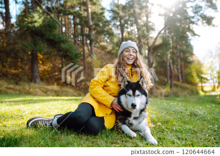 Beautiful young woman in a hat and yellow coat walks with her husky on the lawn in the park. Beautiful young woman in a hat and yellow coat walks with her husky on the lawn in the park. 120644664