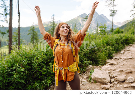 Woman traveler with yellow hiking backpack, hiking poles on trail among mountains. Adventure concept Woman traveler with yellow hiking backpack, hiking poles on trail among mountains. Adventure concept 120644963