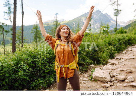 Woman traveler with yellow hiking backpack, hiking poles on trail among mountains. Adventure concept Woman traveler with yellow hiking backpack, hiking poles on trail among mountains. Adventure concept 120644964
