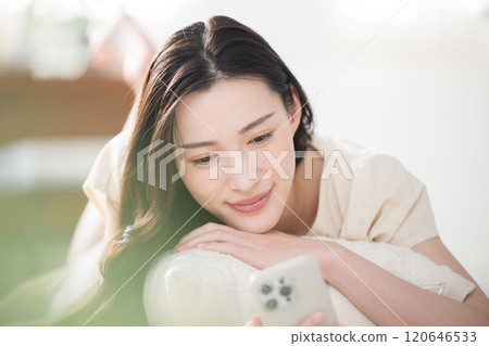 Close-up of a young woman operating a smartphone in bed or in the living room after waking up Close-up of a young woman operating a smartphone in bed or in the living room after waking up 120646533