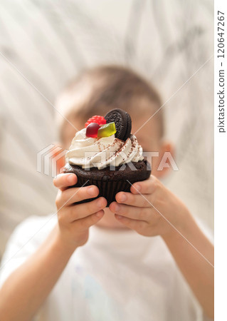The boy holds a mini cake in his hands. The boy holds a mini cake in his hands. 120647267