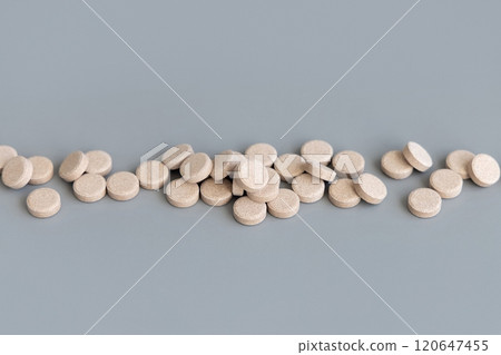 Pile of beige herbal pills in a line on grey close up. Taking dietary supplements and vitamin 120647455