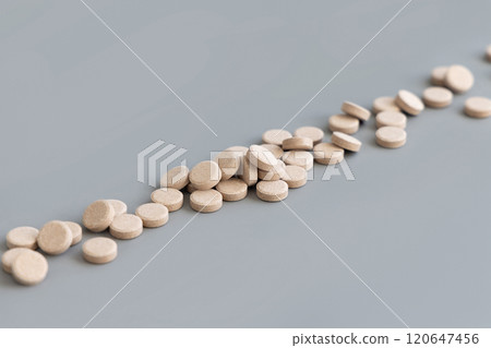 Pile of beige herbal pills in a line on grey close up. Taking dietary supplements and vitamin Pile of beige herbal pills in a line on grey close up. Taking dietary supplements and vitamin 120647456