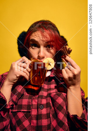 Portrait of young red haired woman sipping mulled wine endearing gingerbread cooking again bright yellow background. Taste of winter 120647808