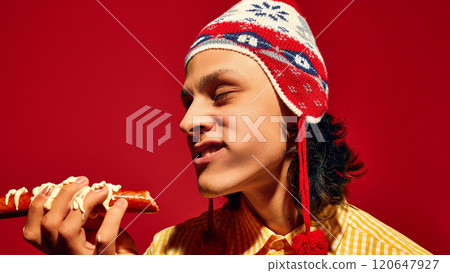 Wow, delicious. Positive, happy,young man in winter hair eating sausage, Bratwurst with mayonnaise sauce against vivid red background 120647927