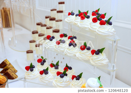 An elegant dessert table features tiers of whipped cream topped with fresh berries at beautifully decorated event atmosphere for guests. An elegant dessert table features tiers of whipped cream topped with fresh berries at beautifully decorated event atmosphere for guests. 120648120