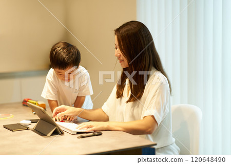 A child playing next to his mother while she is working remotely A child playing next to his mother while she is working remotely 120648490