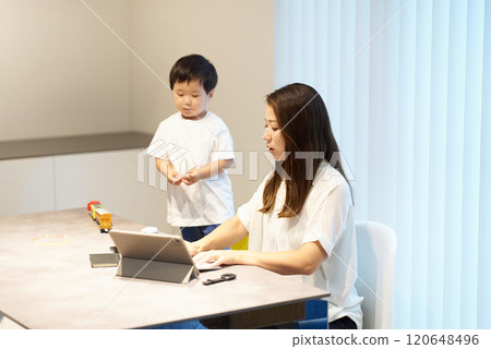 A child playing next to his mother while she is working remotely A child playing next to his mother while she is working remotely 120648496