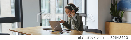 Woman at desk with laptop and headphones, surrounded by houseplants in nice modern coworking office 120648520