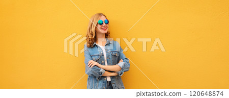 Stylish beautiful happy young woman with crossed arms in denim jacket posing on yellow background 120648874