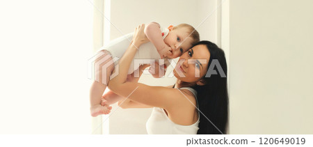 Happy smiling young mother playing with baby in white room at home Happy smiling young mother playing with baby in white room at home 120649019