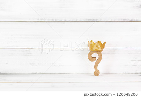 Royal Inquiry: Wooden Question Mark Crowned with Gold Against a Rustic White Background 120649206