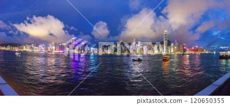 Panoramic nighttime view of illuminated Hong Kong skyline reflected in the water with vibrant city lights 120650355