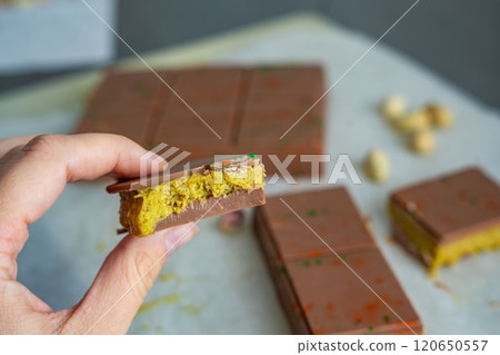 Piece of trend Dubai chocolate with pistachio paste and kataifi dough in woman hand. Confectionery handmade sweets at home in the kitchen.  120650557