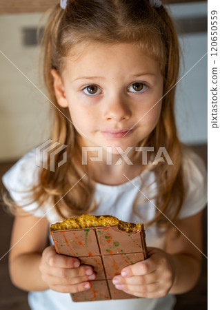 Little girl eating Dubai chocolate with pistachio paste and kataifi dough. Confectionery handmade sweets at home in the kitchen.  120650559