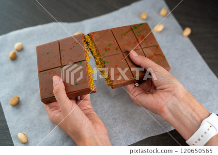 Trend Dubai chocolate with pistachio paste and kataifi dough in woman hands. Confectionery handmade sweets at home in the kitchen.  120650565