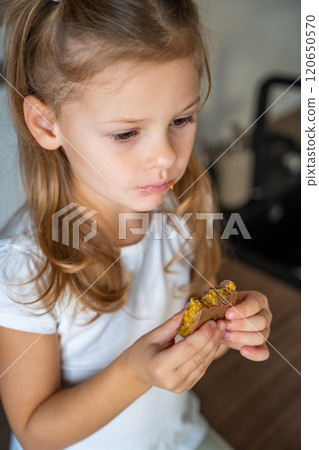 Little girl eating Dubai chocolate with pistachio paste and kataifi dough. Confectionery handmade sweets at home in the kitchen.  120650570