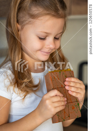 Little girl eating Dubai chocolate with pistachio paste and kataifi dough. Confectionery handmade sweets at home in the kitchen. Little girl eating Dubai chocolate with pistachio paste and kataifi dough. Confectionery handmade sweets at home in the kitchen. 120650578
