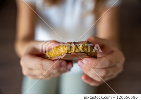 Dubai chocolate with pistachio paste and kataifi dough in hands of little girl. Confectionery handmade sweets at home in the kitchen.  120650580