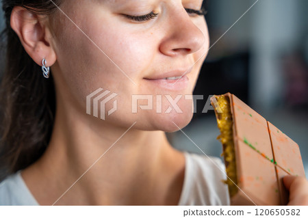 Woman eating trend Dubai chocolate with pistachio paste and kataifi dough. Confectionery handmade sweets at home in the kitchen.  120650582