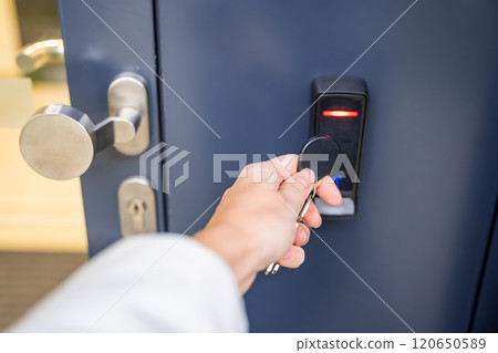 Close up view of person using a electric lock key fob to access a building via a reader of entry system mounted on a house wall 120650589