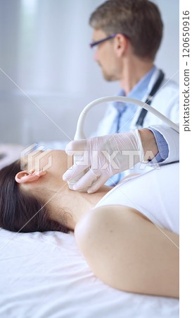 Doctor man wearing white protective gloves is using ultrasound equipment on the neck of patient woman, lying for examination. Medicine concept 120650916