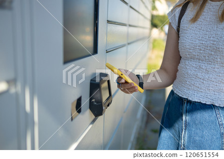 Woman using automated self service post terminal machine or locker to deposit the parcel for storage 120651554