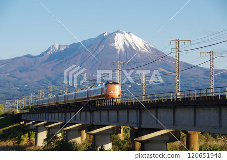 The rear view of the latest 273 series Yakumo 22 express train bound for Okayama, racing across the Hinogawa Bridge at high speed towards the foot of Mt. Oyama, covered in its first snowfall. 120651948
