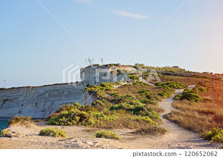 Winding trail meanders through a rocky hill covered with vegetation, bathed in warm golden ligh 120652062