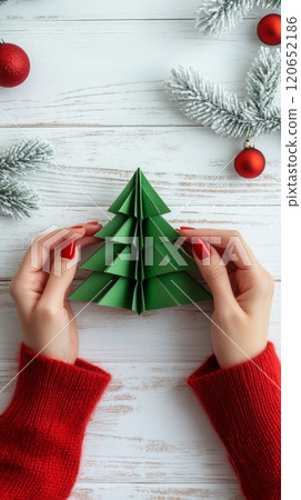 Woman in Red Sweater Making Green Origami Christmas Tree on White Wooden Table, Top View 120652186
