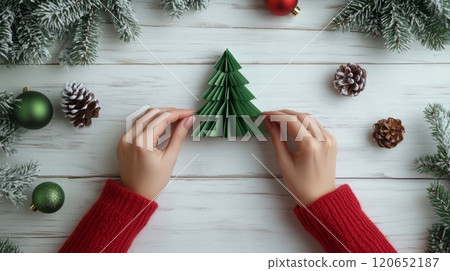 Woman in Red Sweater Creates Festive Decor Crafting an Origami Christmas Tree on White Wooden Table 120652187
