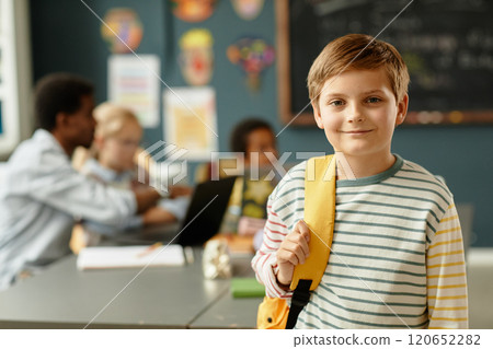 Portrait of adorable young schoolboy in casual clothes wearing backpack smiling sweetly while posing in primary school classroom, copy space Portrait of adorable young schoolboy in casual clothes wearing backpack smiling sweetly while posing in primary school classroom, copy space 120652282