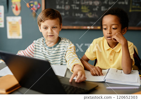 Two boys from different ethnic backgrounds looking at laptop screen browsing information on computer fully engaged in lesson with use of technology in classroom, copy space Two boys from different ethnic backgrounds looking at laptop screen browsing information on computer fully engaged in lesson with use of technology in classroom, copy space 120652303