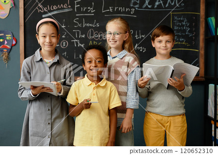 Portrait of four young students from different ethnic backgrounds happily smiling at camera while standing at blackboard in primary school classroom Portrait of four young students from different ethnic backgrounds happily smiling at camera while standing at blackboard in primary school classroom 120652310