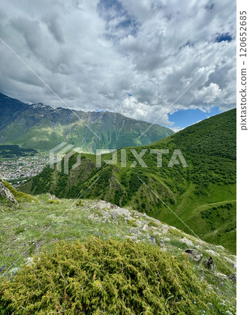 Panoramic view of the Caucasus mountain peaks, meadow and small town scape Panoramic view of the Caucasus mountain peaks, meadow and small town scape 120652685
