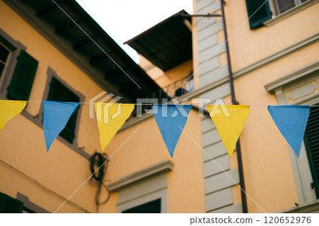 Bunting with colorful triangular flags against old street in Italy. Colored Small triangular waving flags blowing in the wind. High quality photo 120652976