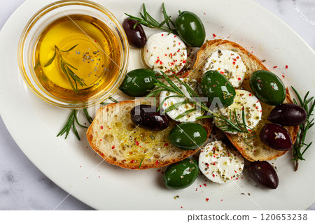 a plate with a snack, ciabatta bread with cheese and olives, olive oil, spices and herbs, top view, no people, 120653238
