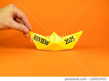 Planning review 2025 new year symbol. Concept words Review 2025 on beautiful yellow paper boat. Beautiful orange paper background. Businessmen hand. Business review 2025 new year concept. Copy space. Planning review 2025 new year symbol. Concept words Review 2025 on beautiful yellow paper boat. Beautiful orange paper background. Businessmen hand. Business review 2025 new year concept. Copy space. 120653435