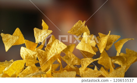 Freeze motion of flying fried tortilla nachos chips on gradient yellow background 120653537